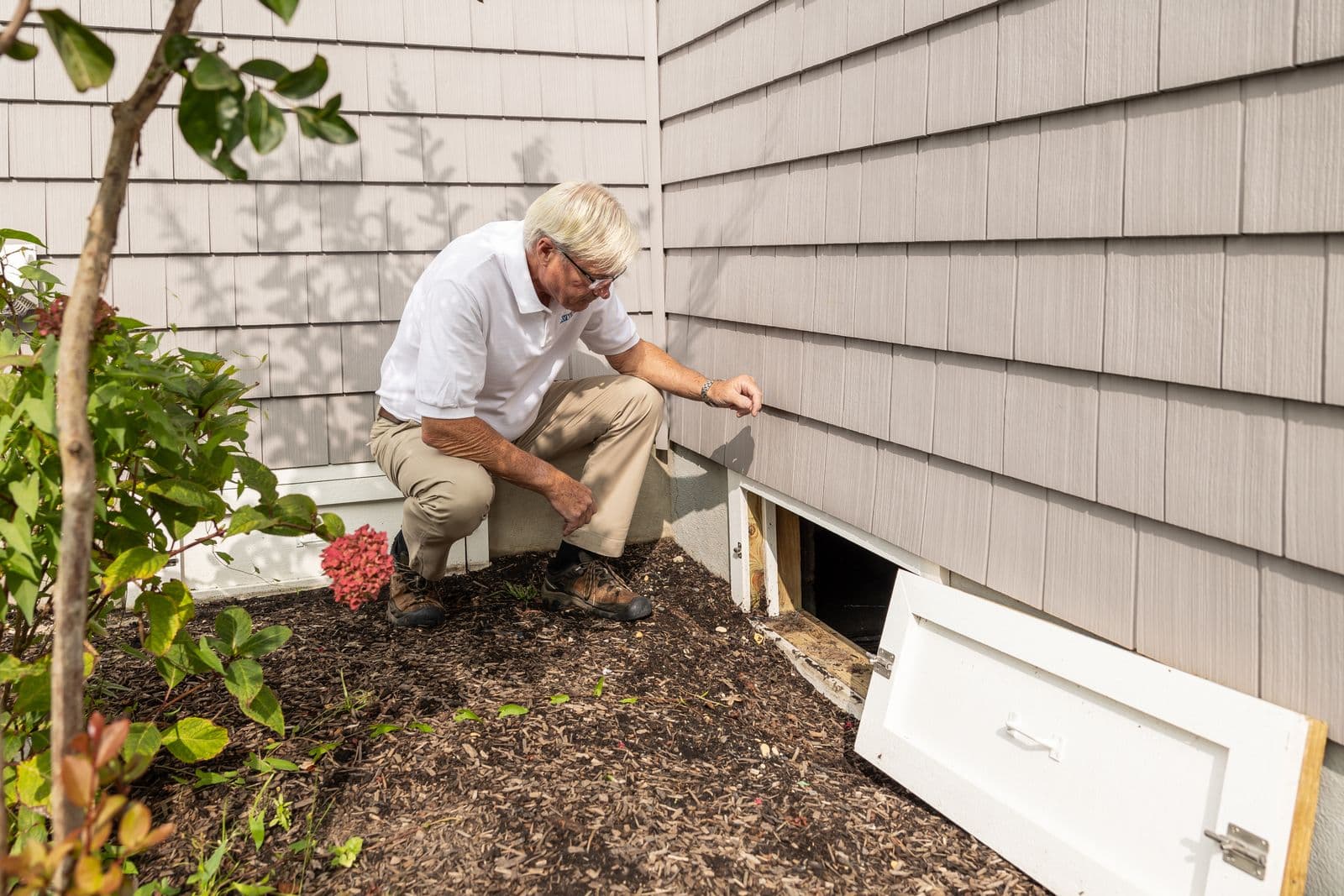 Inspector checking a crawl-space access vent beside a house