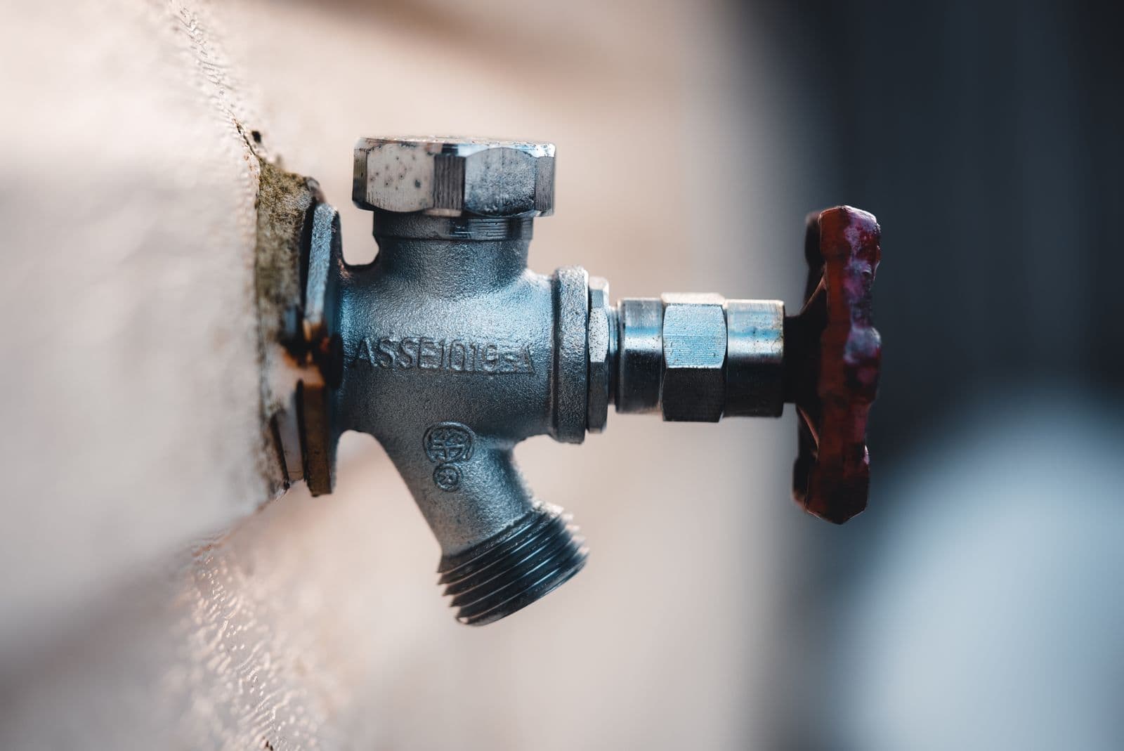 Brass outdoor hose bib with a red handle on an exterior wall
