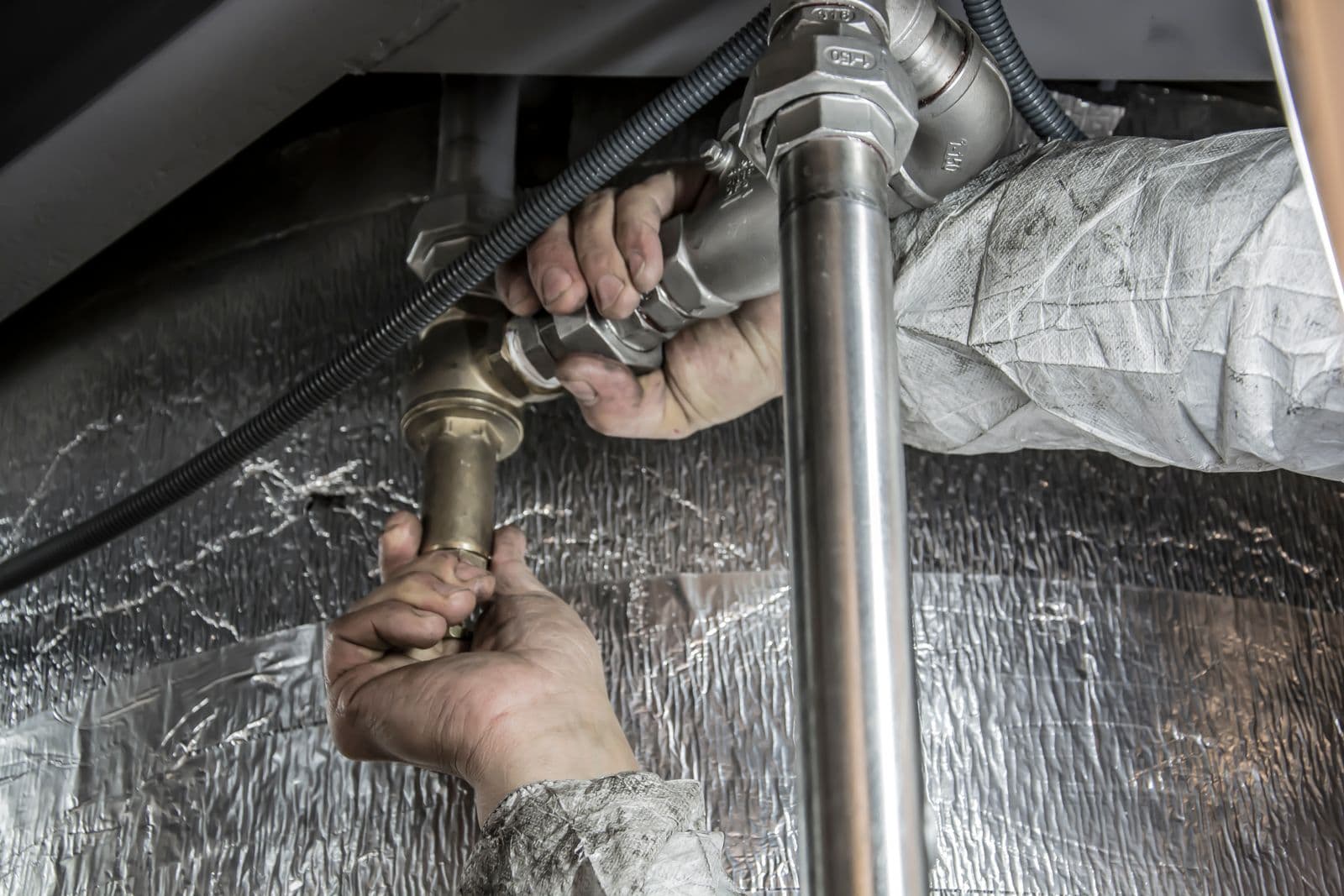 Plumber fitting a supply pipe beneath insulated flooring